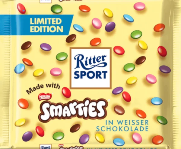 Ritter Sport Smarties al Cioccolato Bianco. Il successo al cioccolato degli anni '90 è tornato. Ricordate il delizioso cioccolato al latte Ritter Sport Smarties? Ora potete finalmente gustare di nuovo questa deliziosa tavoletta. Preparatevi a un sogno di finissimo cioccolato al latte, impreziosito da croccanti Smarties. Le gocce di cioccolato colorate trasformano questa delizia in una delizia colorata e croccante. Questa nuova edizione limitata tanto richiesta fa un grande ritorno SI, ma solamente per un tempo MOLTO LIMITATO.